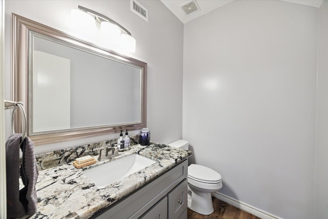 half bath featuring visible vents, baseboards, wood finished floors, and toilet