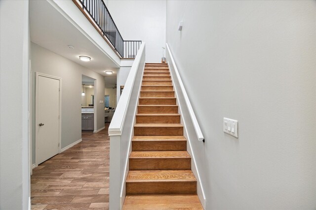 stairs with a high ceiling, wood finished floors, and baseboards