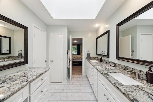 bathroom with marble finish floor, a sink, double vanity, and a skylight