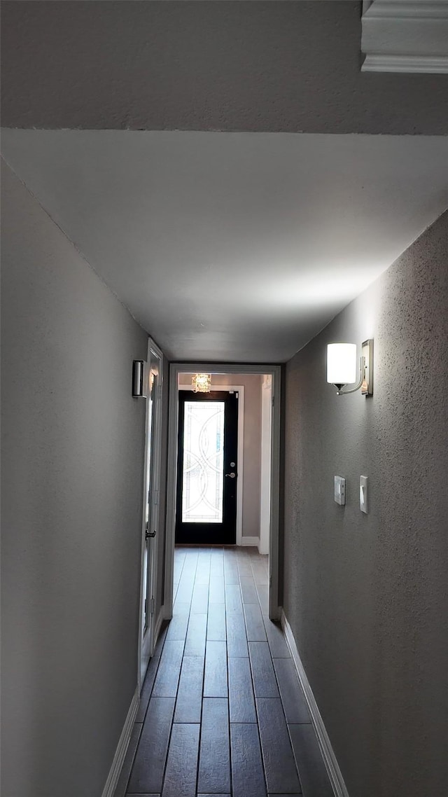 corridor featuring light wood-type flooring, a textured wall, and baseboards