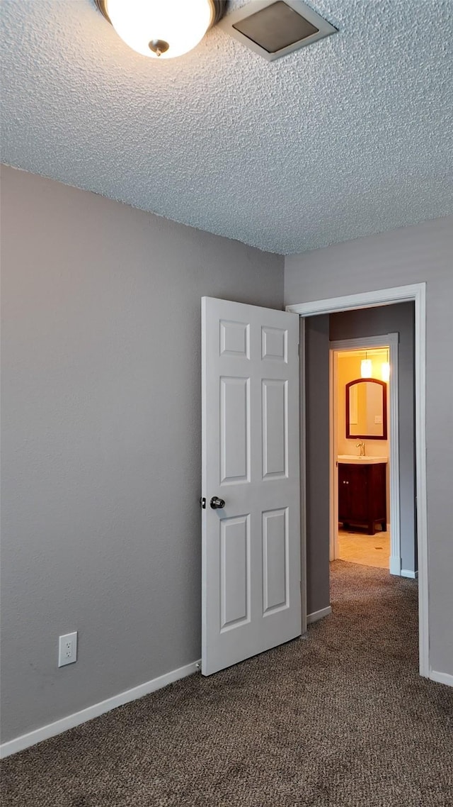 unfurnished room with a textured ceiling, baseboards, and carpet