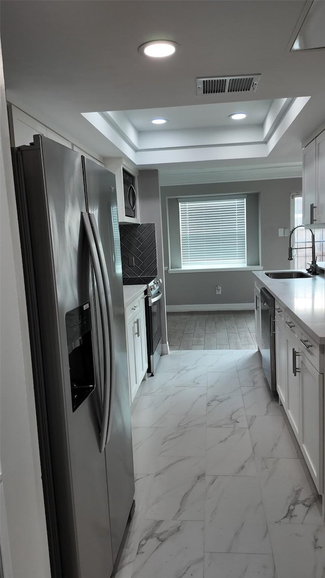 kitchen with white cabinetry, visible vents, a tray ceiling, stainless steel appliances, and a sink