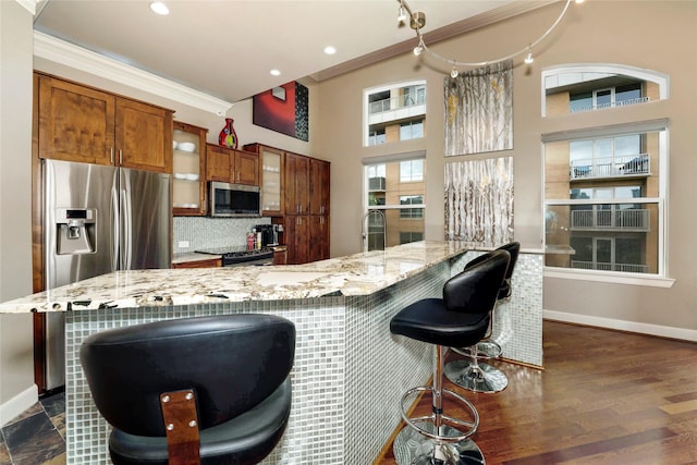 kitchen featuring brown cabinets, baseboards, appliances with stainless steel finishes, and glass insert cabinets