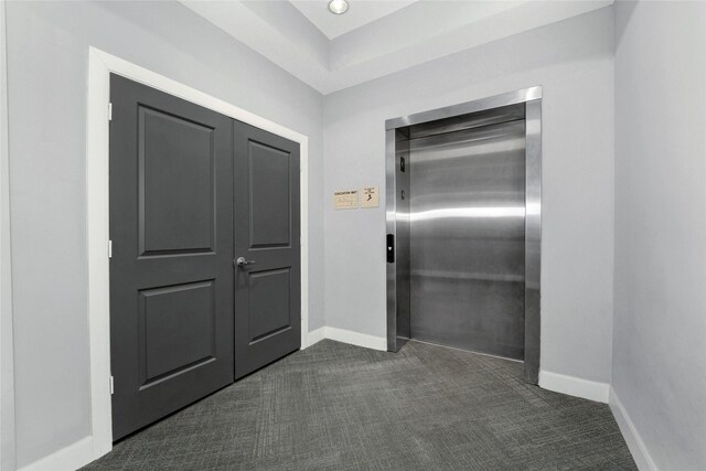 interior space featuring baseboards, elevator, and dark colored carpet