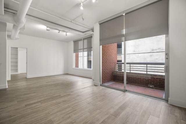 unfurnished room featuring baseboards, track lighting, and wood finished floors