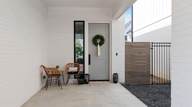 entrance to property featuring fence, a gate, a patio, and brick siding