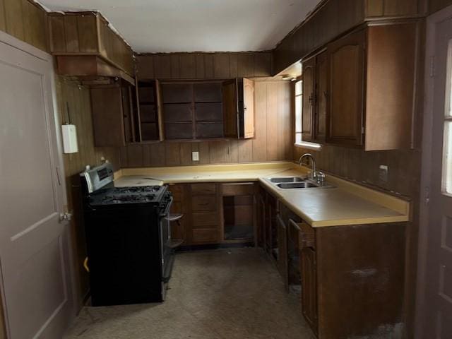 kitchen with stainless steel range with gas stovetop, a sink, wood walls, light floors, and light countertops