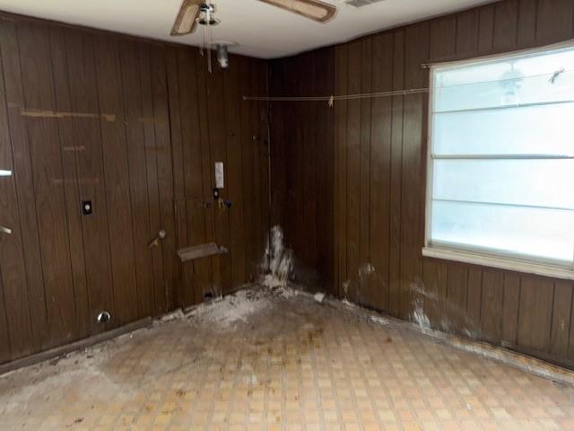 empty room featuring wooden walls, visible vents, and ceiling fan