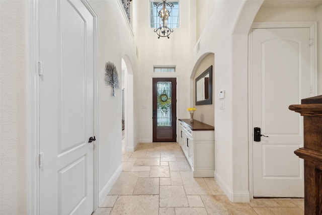 foyer featuring stone tile flooring, baseboards, arched walkways, and a towering ceiling