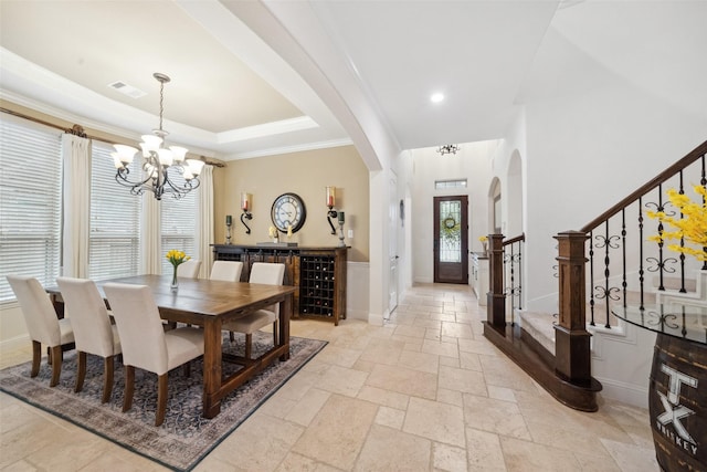 dining space featuring stone tile floors, a chandelier, stairs, a raised ceiling, and arched walkways
