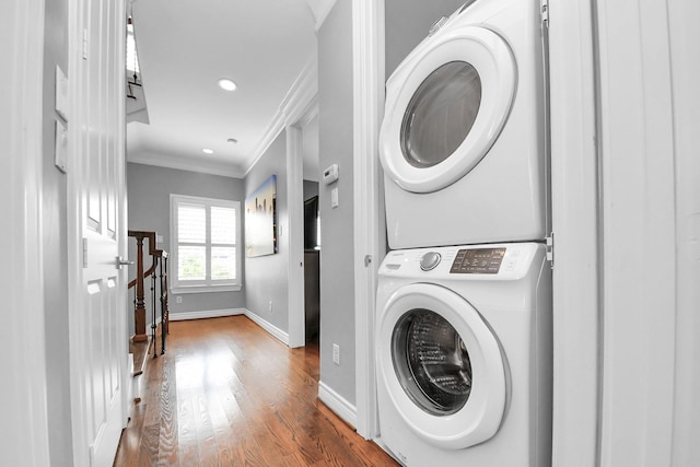 laundry room featuring stacked washer / drying machine, laundry area, baseboards, wood finished floors, and ornamental molding