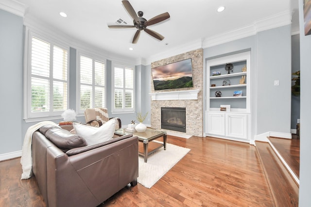 living room featuring crown molding, a fireplace, built in features, a ceiling fan, and baseboards