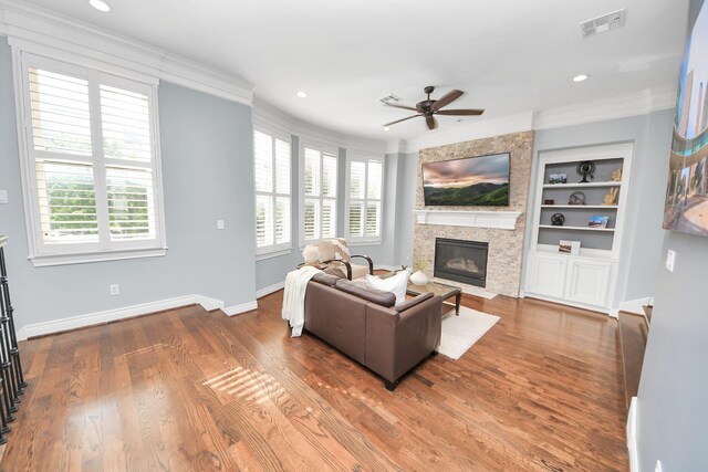 living area featuring a ceiling fan, crown molding, built in features, a fireplace, and baseboards