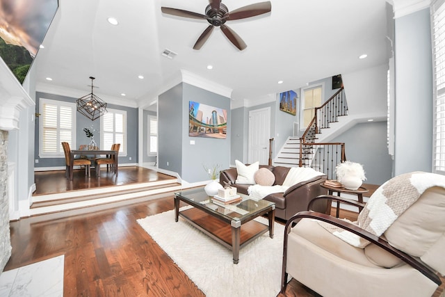 living room featuring a ceiling fan, wood finished floors, visible vents, ornamental molding, and stairway