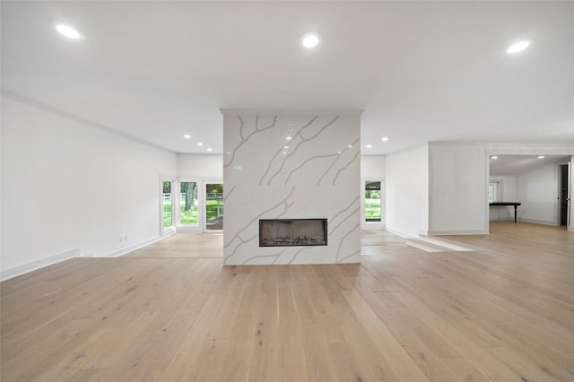 unfurnished living room featuring a high end fireplace, plenty of natural light, light wood finished floors, and baseboards
