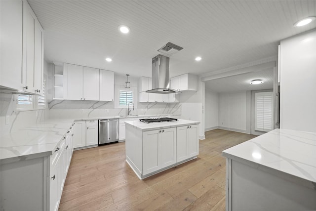 kitchen featuring stainless steel dishwasher, island exhaust hood, a sink, visible vents, and light stone countertops