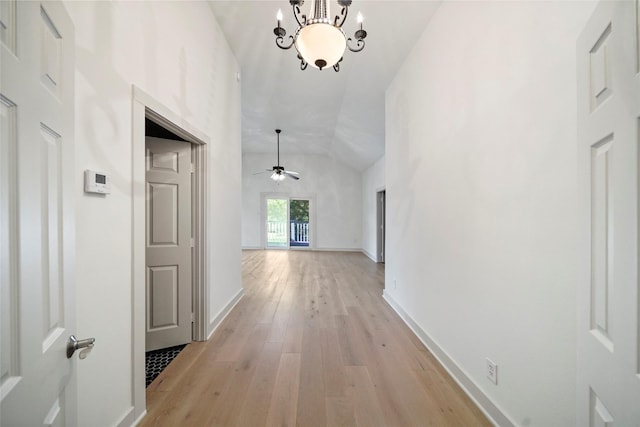corridor with baseboards, vaulted ceiling, and light wood-style flooring