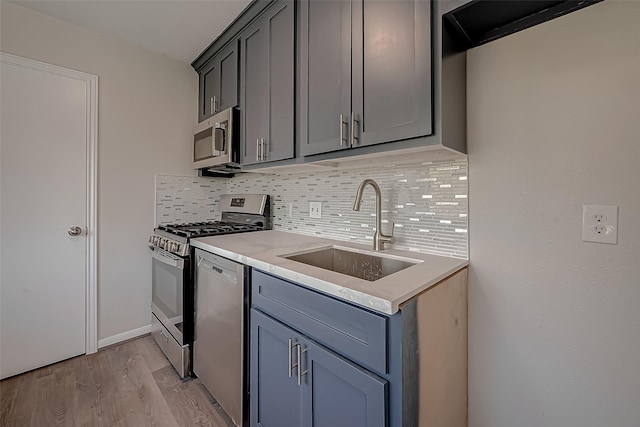2102 Banks St, Houston, TX 77098 - kitchen featuring stainless steel appliances, gray cabinets, a sink, decorative backsplash, and light wood-style flooring