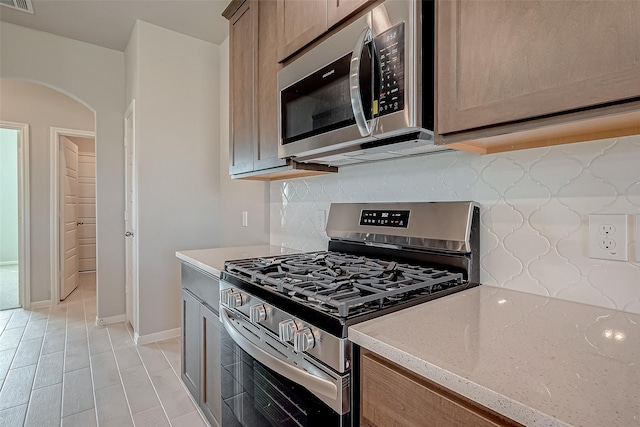 kitchen with stainless steel appliances, arched walkways, visible vents, decorative backsplash, and light stone countertops