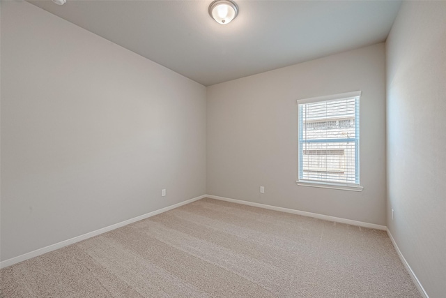 spare room with baseboards and light colored carpet