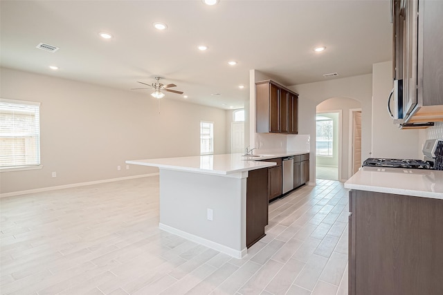 kitchen with a peninsula, arched walkways, a ceiling fan, light countertops, and appliances with stainless steel finishes