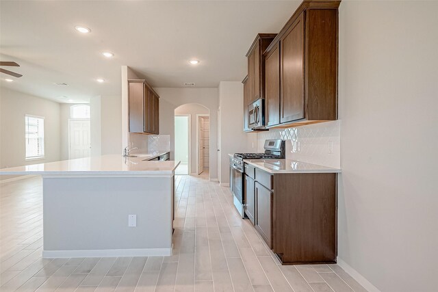 kitchen featuring arched walkways, backsplash, appliances with stainless steel finishes, and ceiling fan