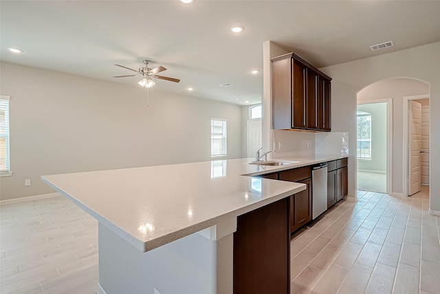 kitchen with a ceiling fan, stainless steel dishwasher, a sink, arched walkways, and a peninsula
