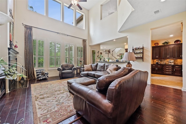 living area with a ceiling fan, visible vents, a high ceiling, and dark wood-style flooring