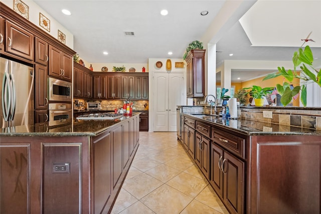 kitchen with a sink, dark stone counters, light tile patterned flooring, decorative backsplash, and appliances with stainless steel finishes