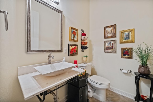 half bath with tile patterned flooring, toilet, baseboards, and a sink
