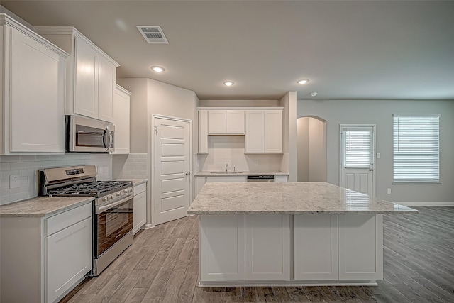 2128 Port Jackson, Texas City, TX 77568 - kitchen with stainless steel appliances, arched walkways, a kitchen island, light wood-style flooring, and white cabinetry
