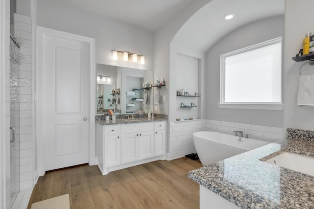 bathroom featuring a soaking tub, wood finished floors, two vanities, and a sink