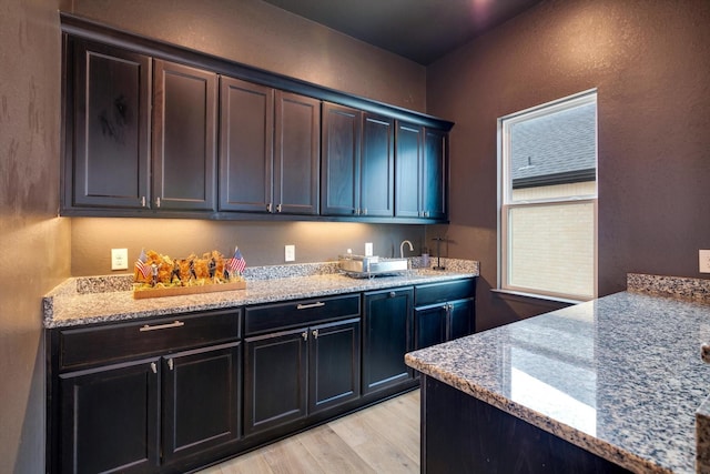 kitchen with light wood-style floors, a textured wall, and light stone counters