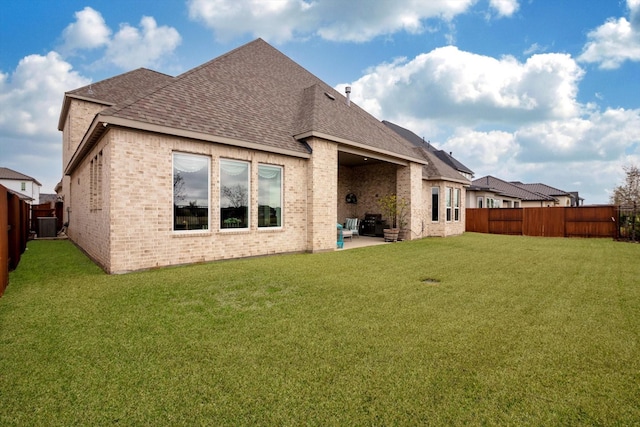 back of house with a fenced backyard, brick siding, a patio, and a lawn