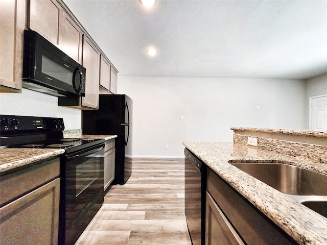kitchen with baseboards, recessed lighting, light wood-style floors, light stone countertops, and black appliances