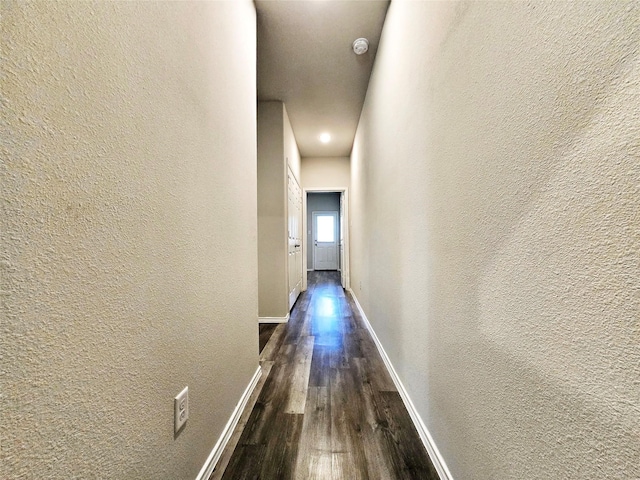 hall with baseboards, a textured wall, and dark wood-style floors