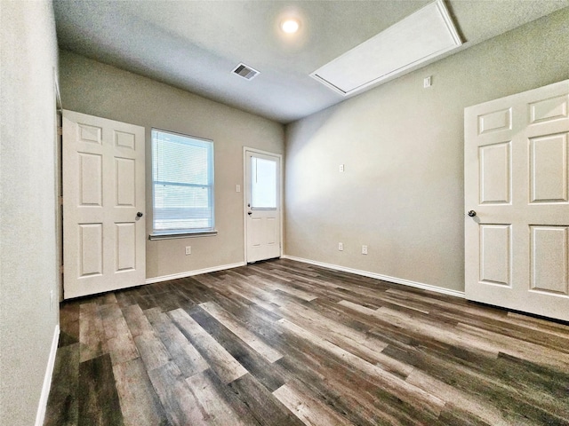 unfurnished room featuring attic access, dark wood finished floors, visible vents, and baseboards