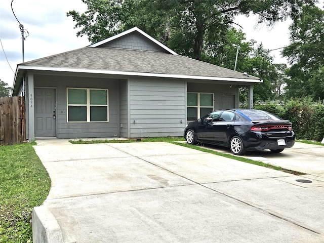 view of front of house featuring a shingled roof, concrete driveway, and fence