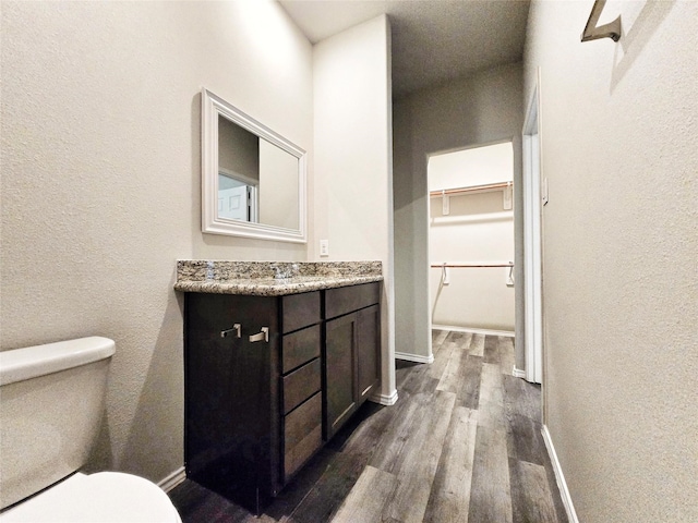 bathroom with toilet, baseboards, wood finished floors, a textured wall, and vanity