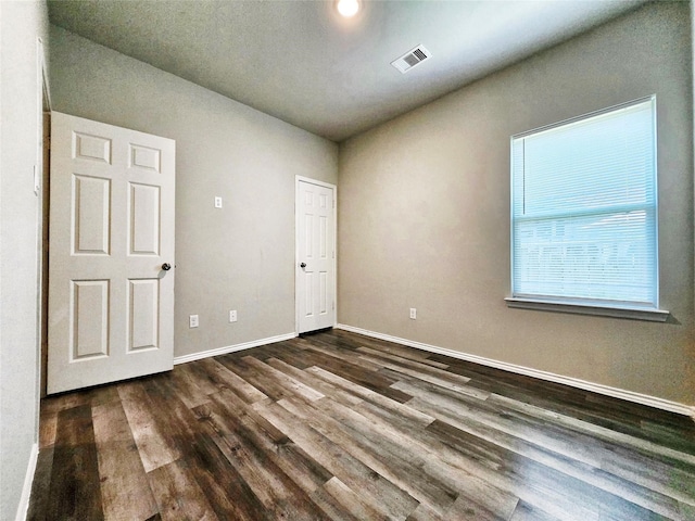 unfurnished room featuring dark wood finished floors, visible vents, and baseboards