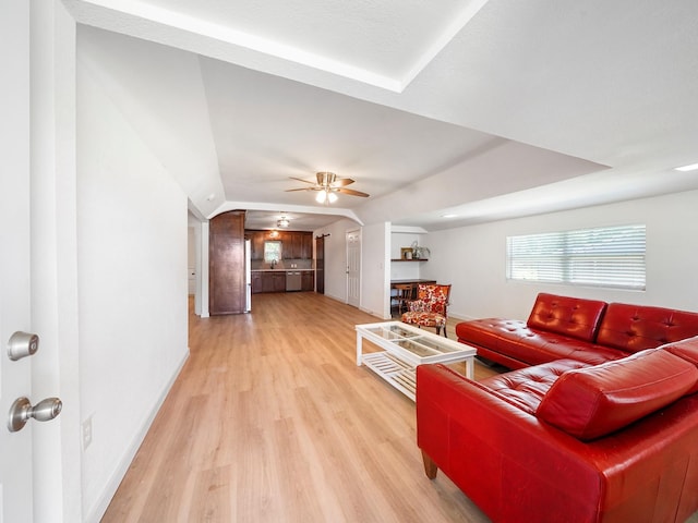 living room featuring baseboards, light wood-type flooring, a ceiling fan, and vaulted ceiling