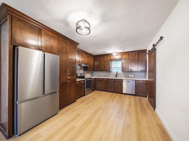 kitchen featuring a sink, decorative backsplash, light wood-style floors, light countertops, and appliances with stainless steel finishes