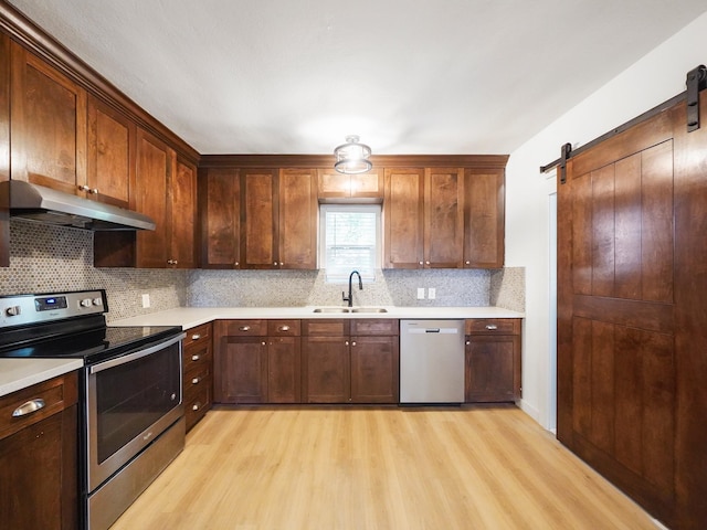kitchen with a sink, a barn door, under cabinet range hood, light wood-style flooring, and appliances with stainless steel finishes