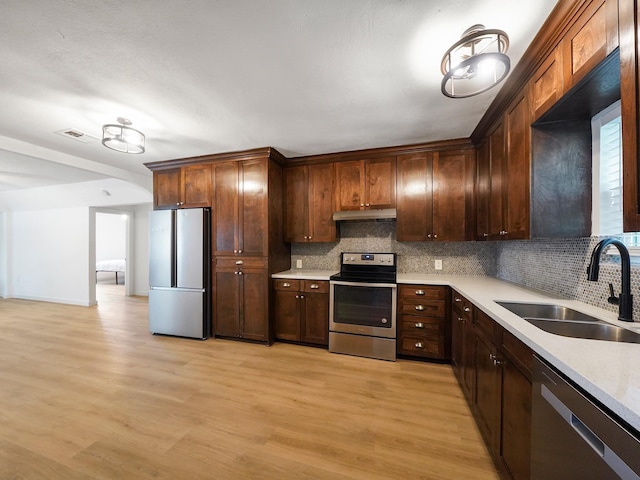 kitchen with appliances with stainless steel finishes, light countertops, decorative backsplash, and a sink