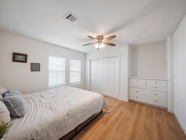 bedroom with a closet, a ceiling fan, visible vents, light wood-style flooring, and baseboards