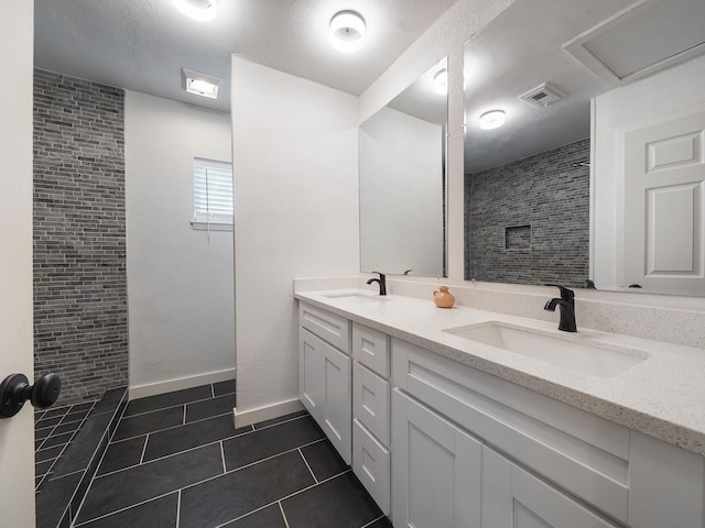 bathroom featuring a sink, tiled shower, tile patterned floors, and visible vents