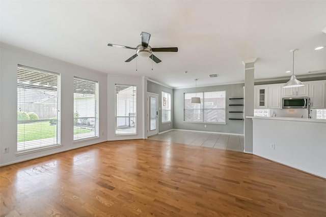 unfurnished living room featuring light wood finished floors, baseboards, ceiling fan, and crown molding