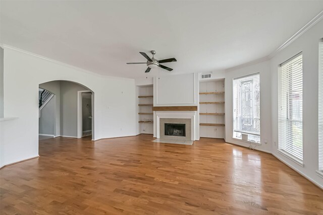 unfurnished living room featuring arched walkways, a healthy amount of sunlight, visible vents, a ceiling fan, and crown molding