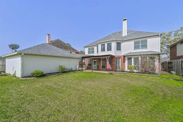 rear view of house featuring a chimney, fence, brick siding, a lawn, and a patio