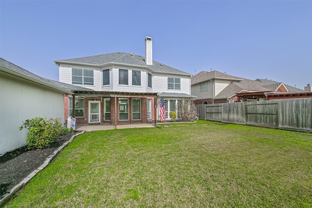 rear view of house featuring a chimney, a fenced backyard, a yard, a patio, and brick siding